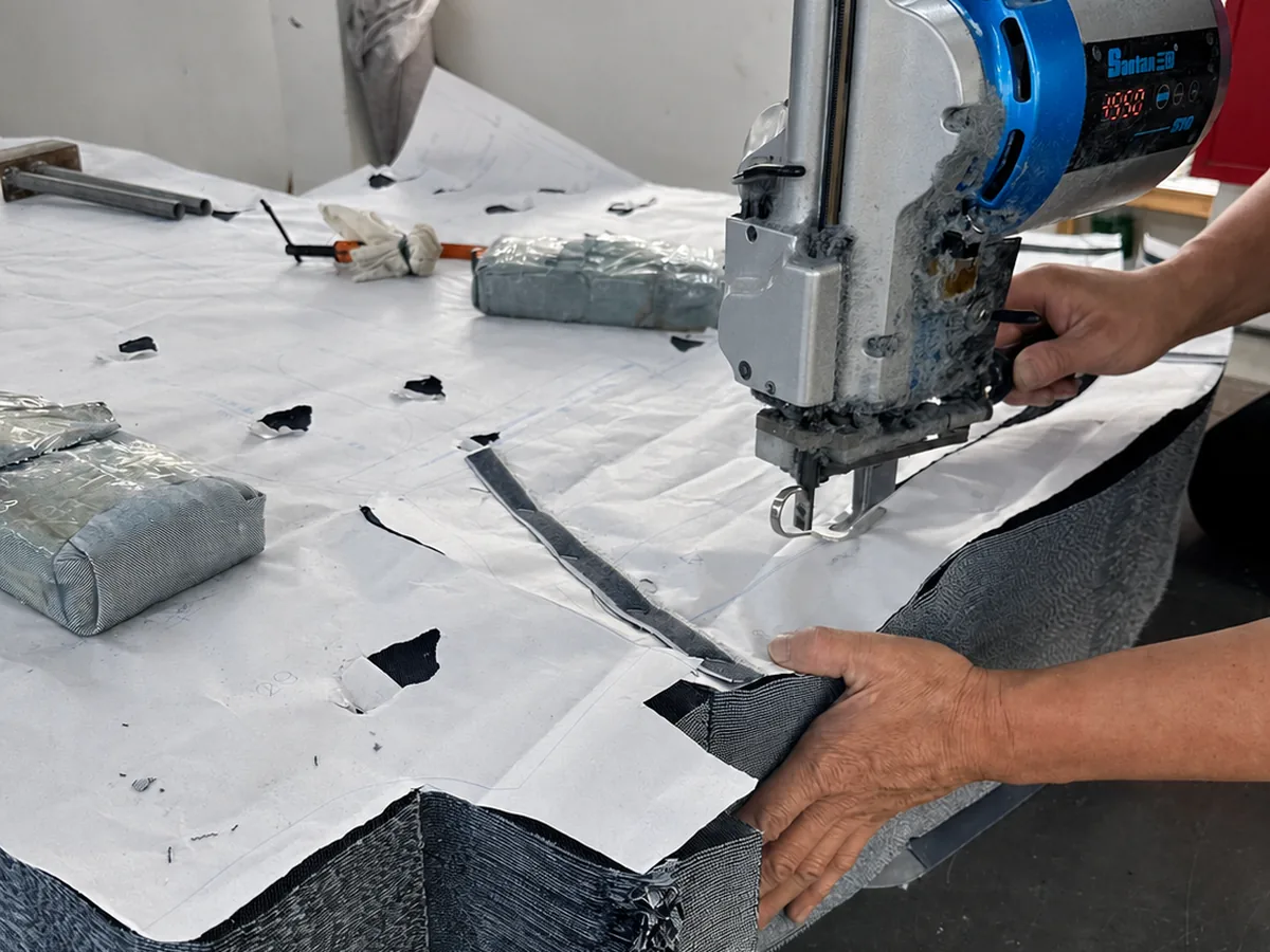 Worker cutting stacked denim fabric with paper patterns in a garment factory