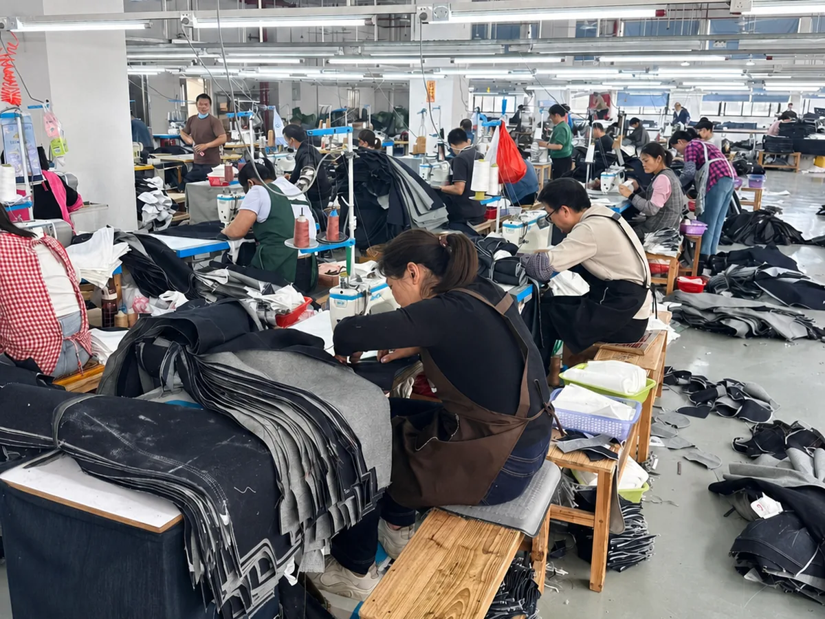 Workers sewing denim garment panels on a factory production line