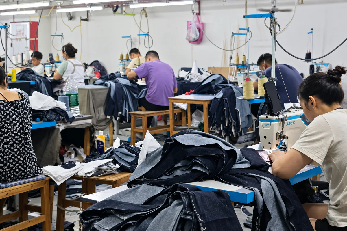 Denim sewing workshop with workers producing garments on industrial sewing machines