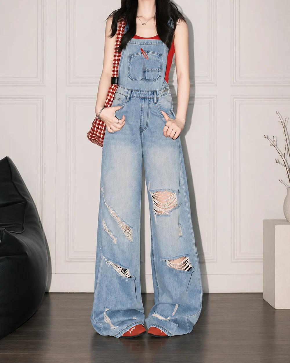 Faceless model wearing ripped light-wash wide-leg denim overalls with an oversized relaxed fit