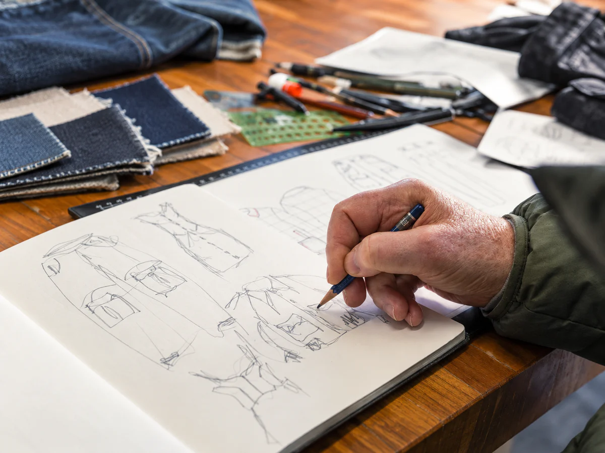 Designer sketching an early denim garment concept in a notebook