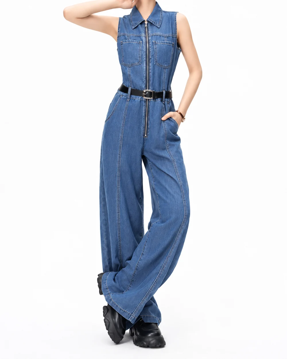 Faceless model wearing a belted zip-front denim jumpsuit with chest pockets and wide legs